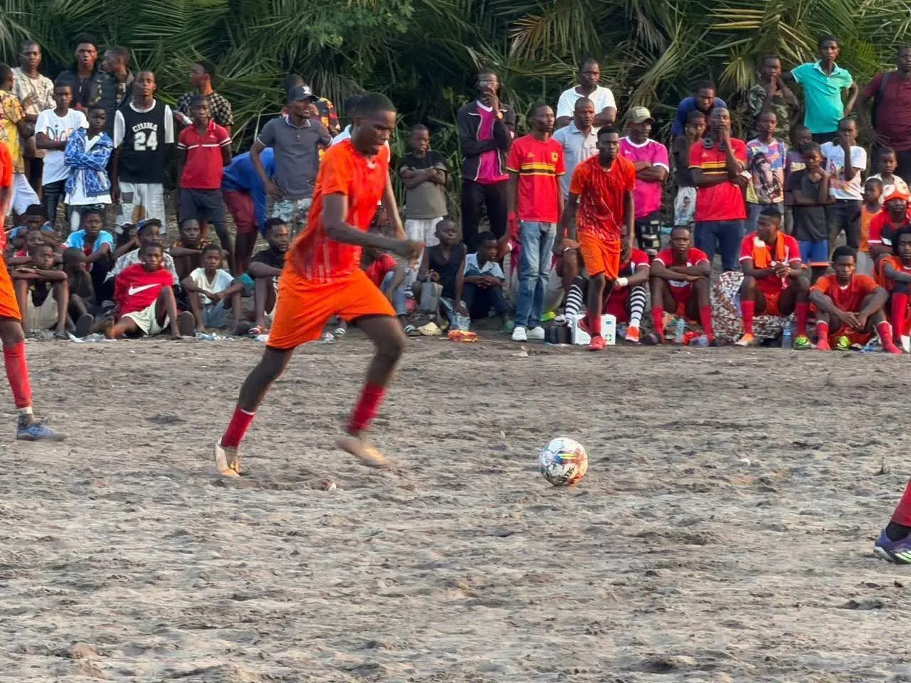 Jogo de futebol em campo de areia com adeptos a assistir